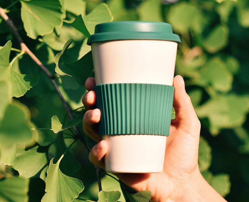 Hand holding eco-friendly reusable coffee cup against green background